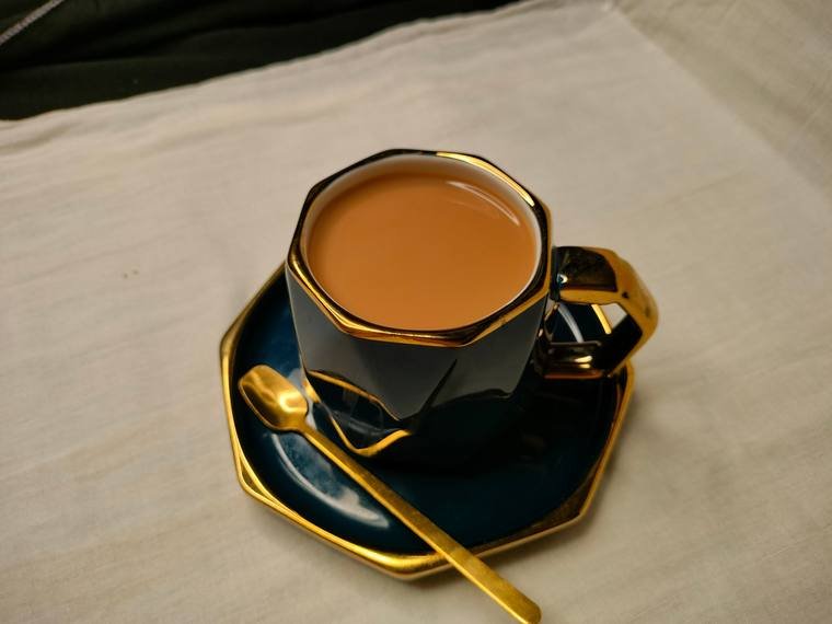 Chai in a black and gold cup on a dark set, product photography by Propix Jaipur
