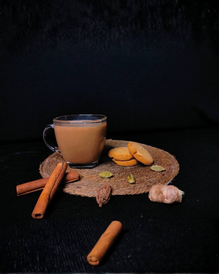 Chai styled with cinnamon, cardamom and biscuits on a dark set, product photography by Propix
